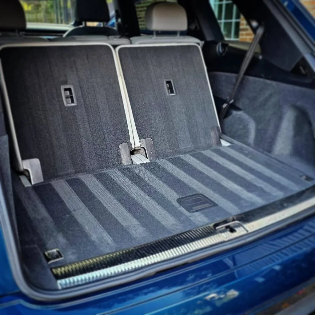 Open cargo area of a blue SUV showing freshly cleaned dark gray carpet with vacuum lines and folded rear seat backs