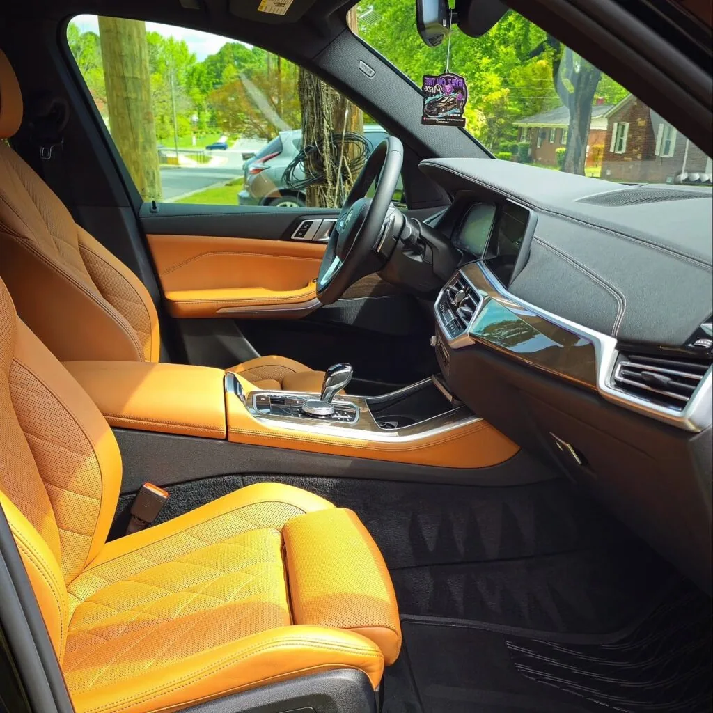 BMW SUV front cabin with clean quilted tan leather seats, black dash, and vacuumed floor mats after interior detailing