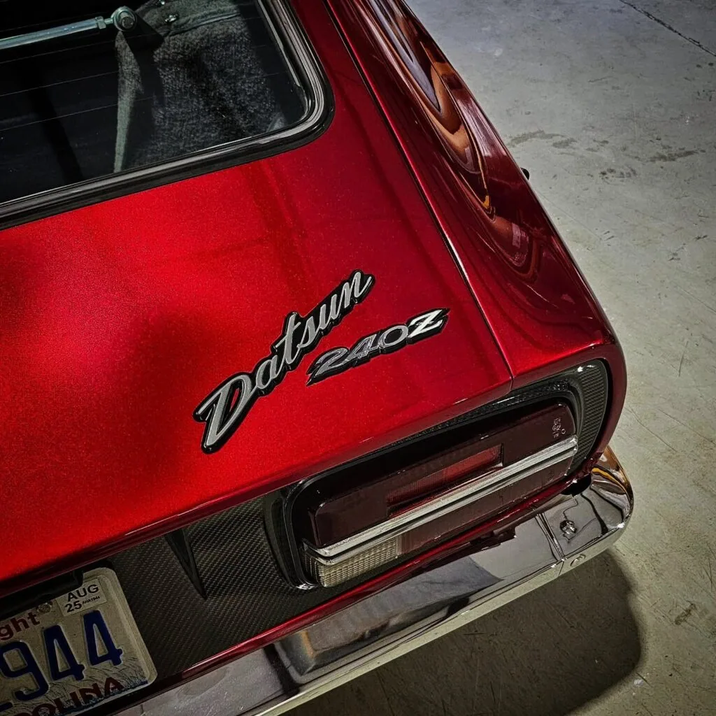 Close-up of candy red Datsun 240Z rear panel showing chrome badges, taillight, and polished chrome bumper.
