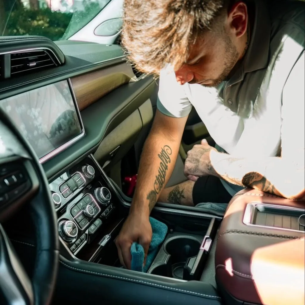 Detailer wipes an SUV cupholder and center console with a blue microfiber towel during interior cleaning.