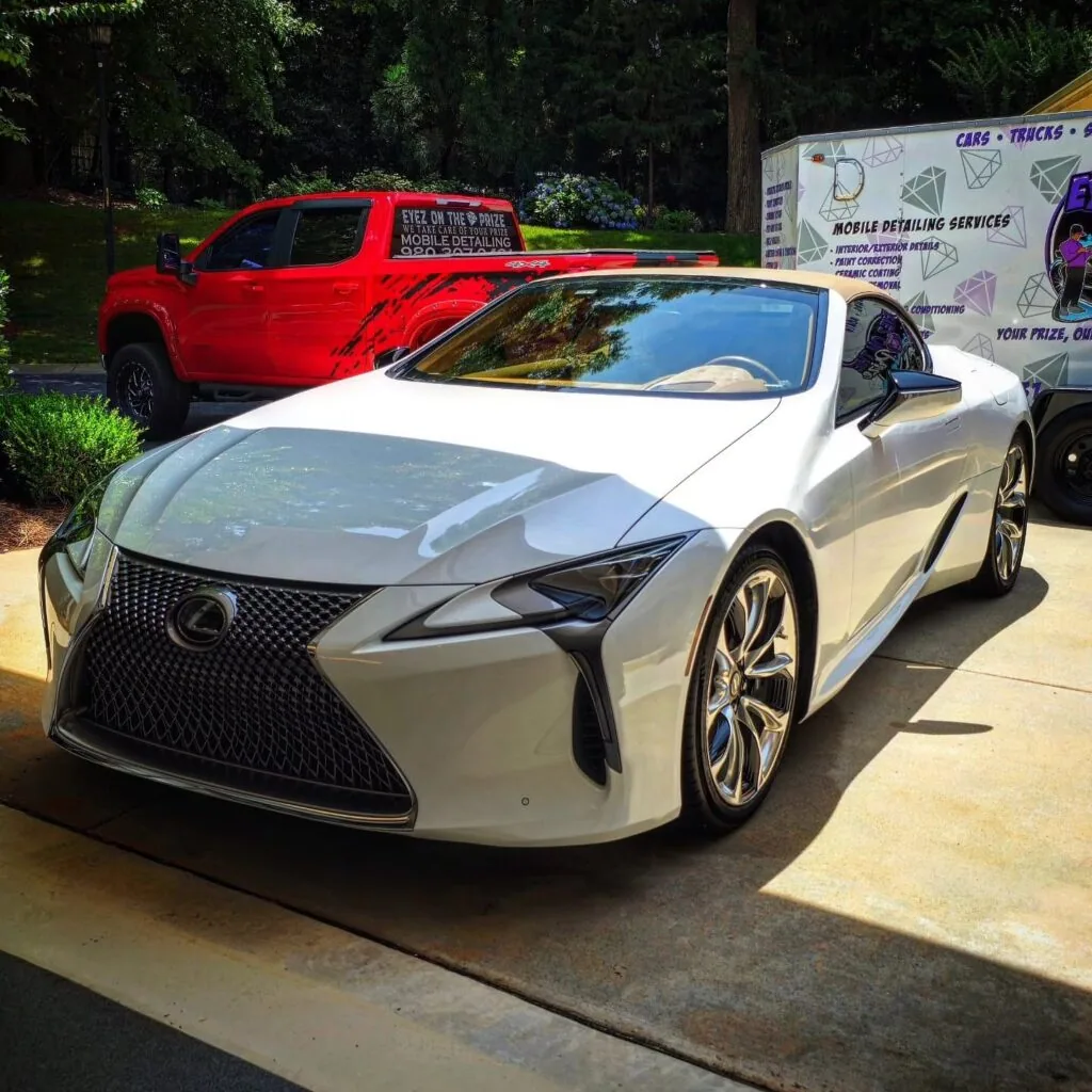 White Lexus LC 500 convertible with tan soft top parked on a driveway, Eyez On The Prize detailing truck and trailer behind