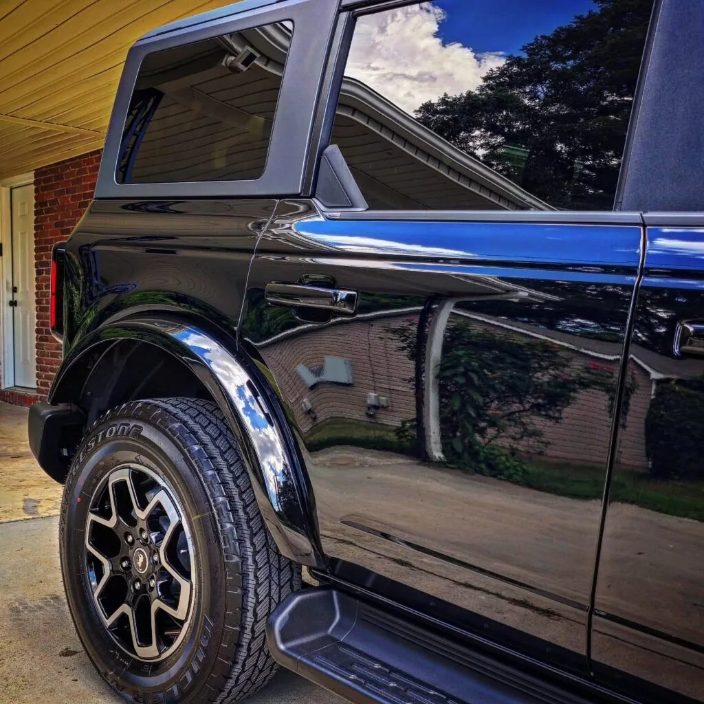 Side view of a black Ford Bronco showing glossy rear door, fender flare, and Bridgestone tire in a driveway