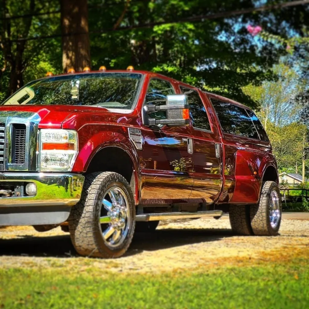Low front quarter view of a maroon Ford Super Duty crew cab truck with glossy paint and chrome wheels on a gravel driveway