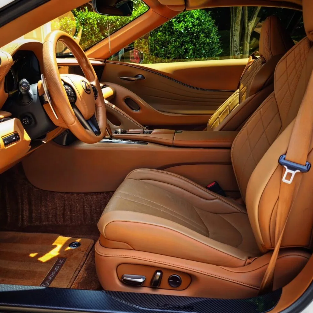 Driver side interior of a Lexus LC with clean tan leather seats, steering wheel, and vacuumed brown carpet.