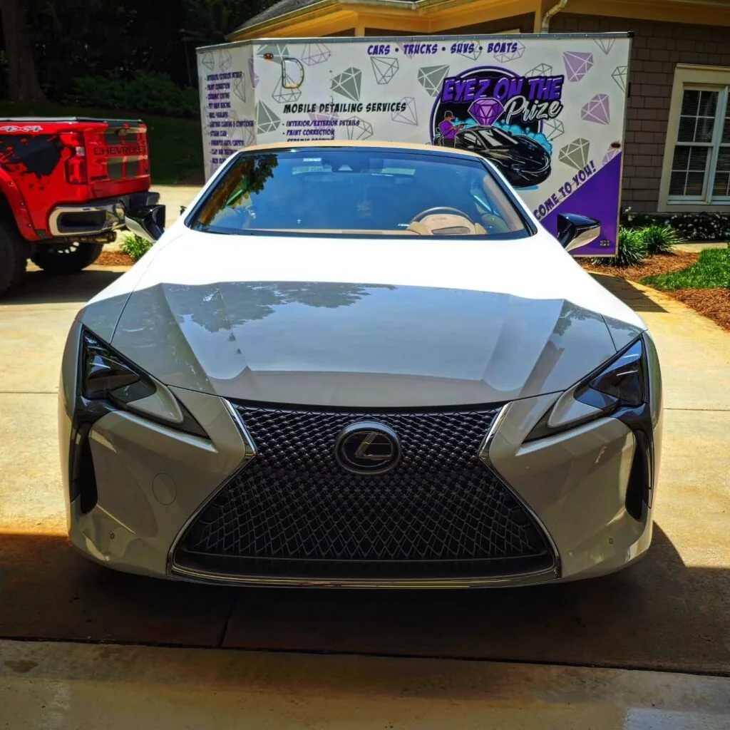 Front view of a white Lexus LC convertible parked in front of an Eyez On The Prize Auto Spa mobile detailing trailer