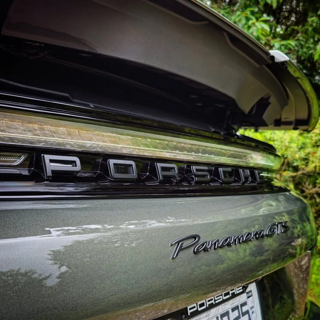 Close-up of the rear Porsche Panamera GTS badging and light bar on a glossy gray-green sedan with the trunk open.