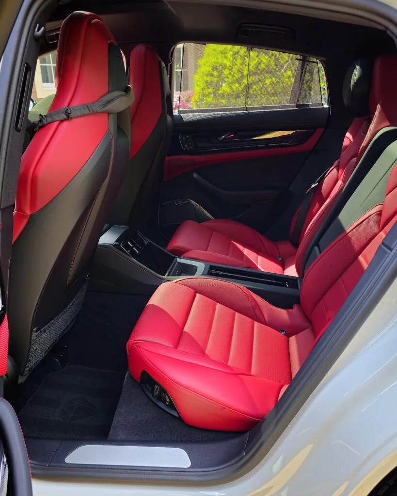 Rear cabin of a Porsche Panamera with cleaned red leather seats, black carpet, and door panel viewed through the open door.