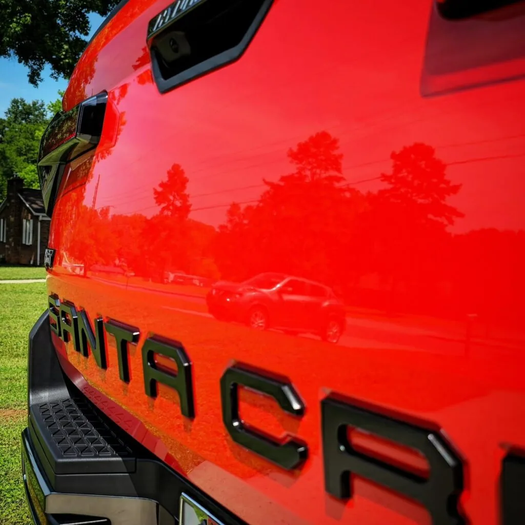 Close-up of a red Hyundai Santa Cruz tailgate with glossy paint reflecting trees and a passing car