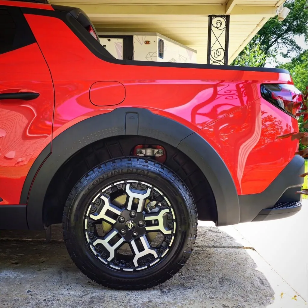 Close-up of the rear wheel and fender of a red Hyundai Santa Cruz with a cleaned two-tone alloy wheel and dressed Continental