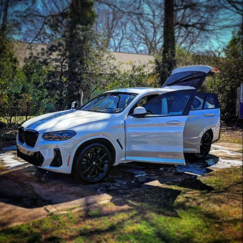White BMW SUV with doors and liftgate open on a driveway with soap suds during a mobile detailing wash in Charlotte, NC.