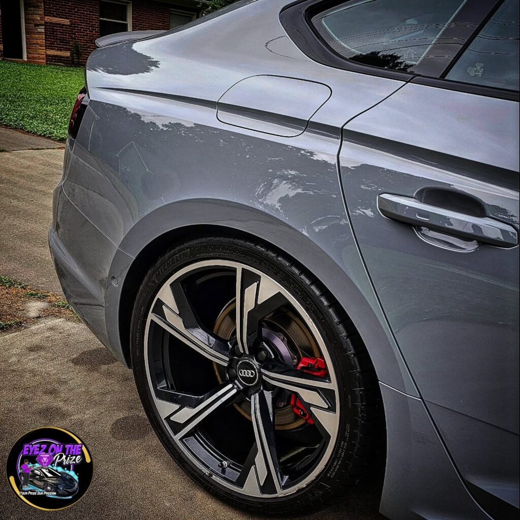 Close-up of a gray Audi RS5 rear wheel with red brake caliper and glossy rear quarter panel after detailing