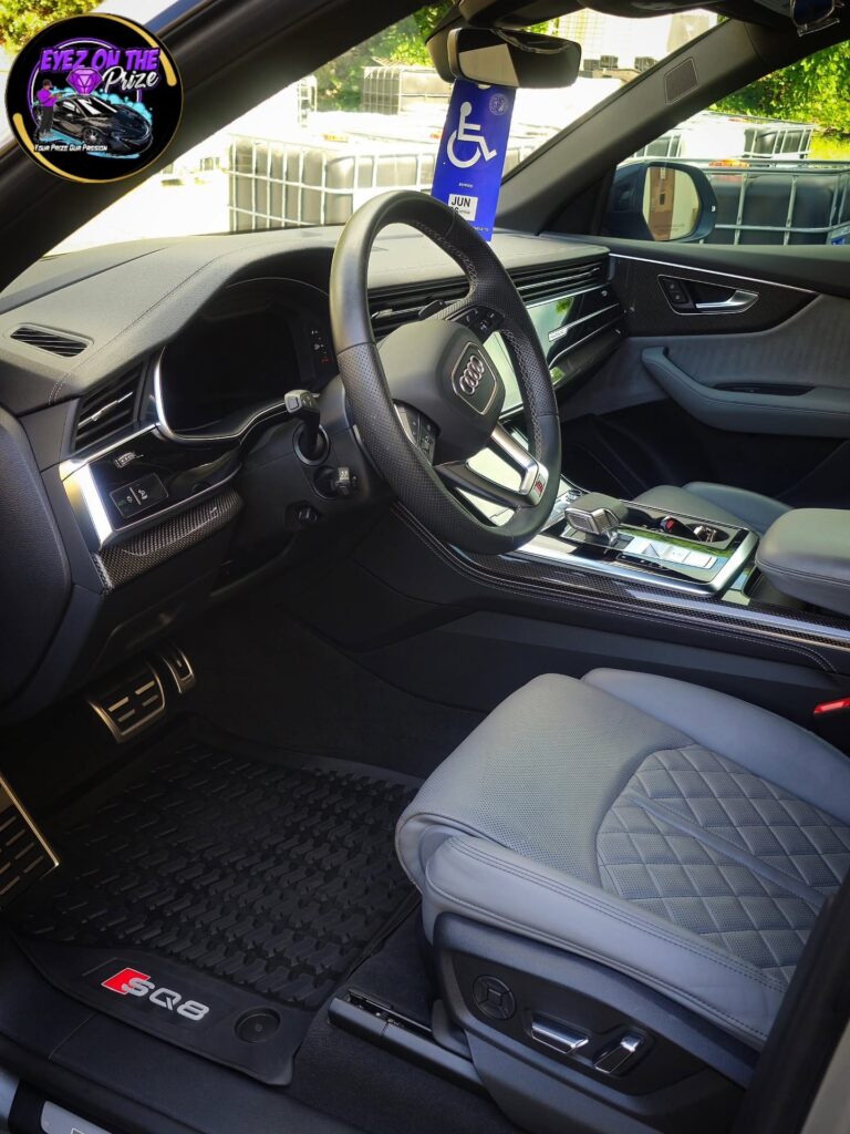 Audi SQ8 driver cockpit with gray diamond-stitched leather seat, clean steering wheel, and SQ8 floor mat after detailing.