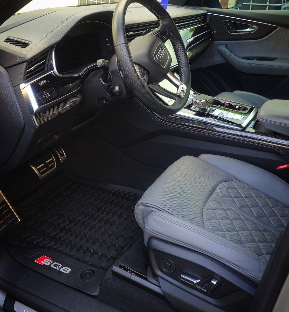 Audi SQ8 driver cockpit with gray diamond-stitched leather seat, clean steering wheel, and SQ8 floor mat after detailing.