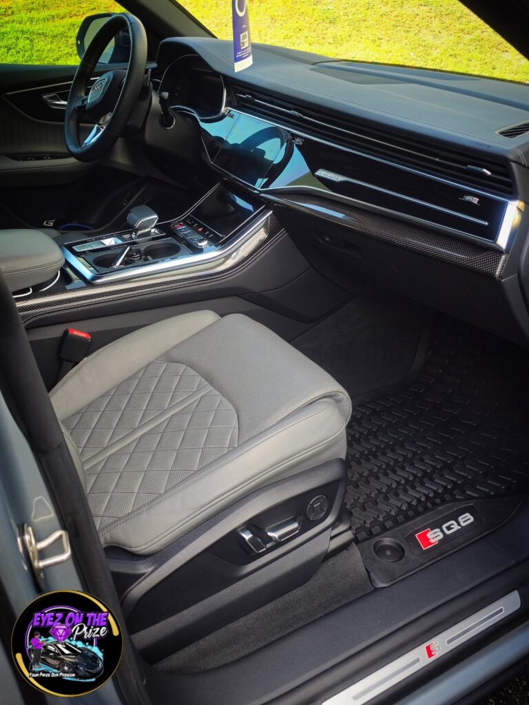 Passenger side interior of an Audi SQ8 with gray diamond-stitched leather seat, clean dashboard, and SQ8 rubber floor mat.