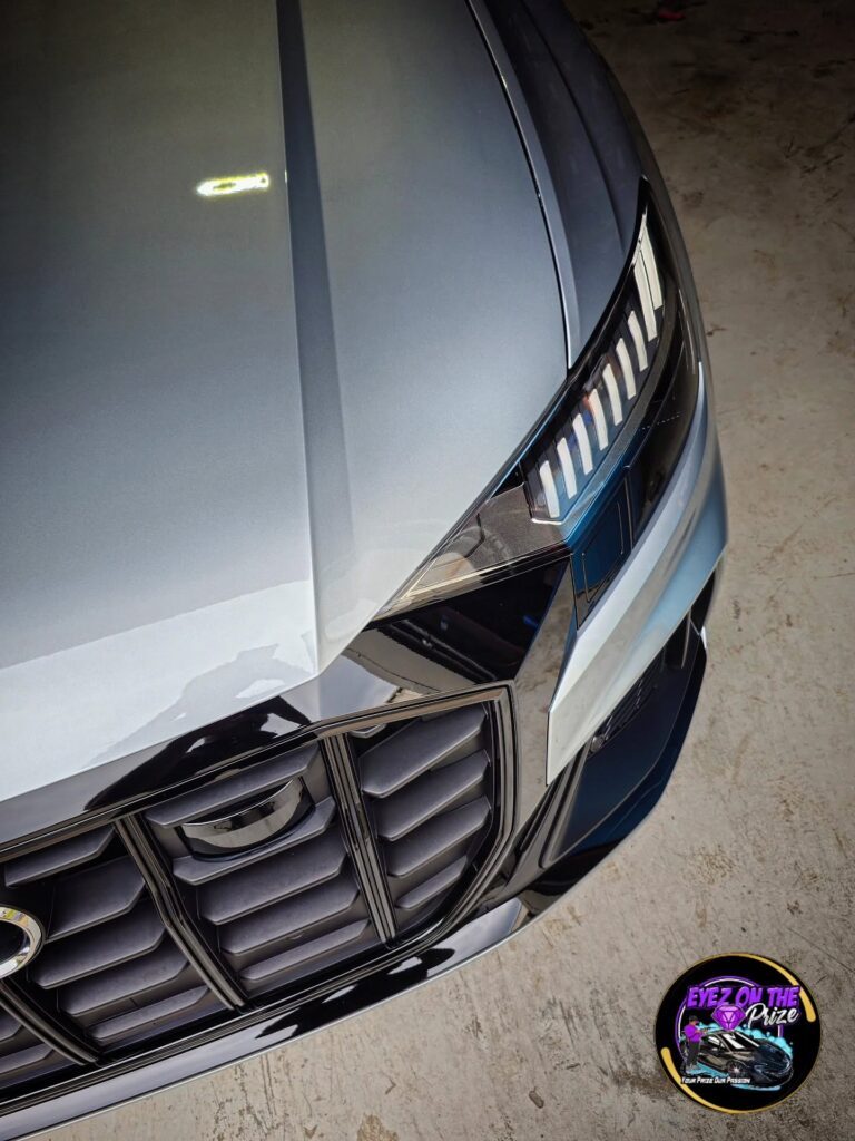Overhead close-up of a gray Audi SQ8 hood, LED headlight, and black grille with a glossy polished finish