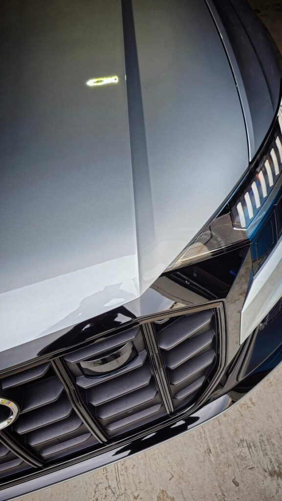 Overhead close-up of a gray Audi SQ8 hood, LED headlight, and black grille with a glossy polished finish