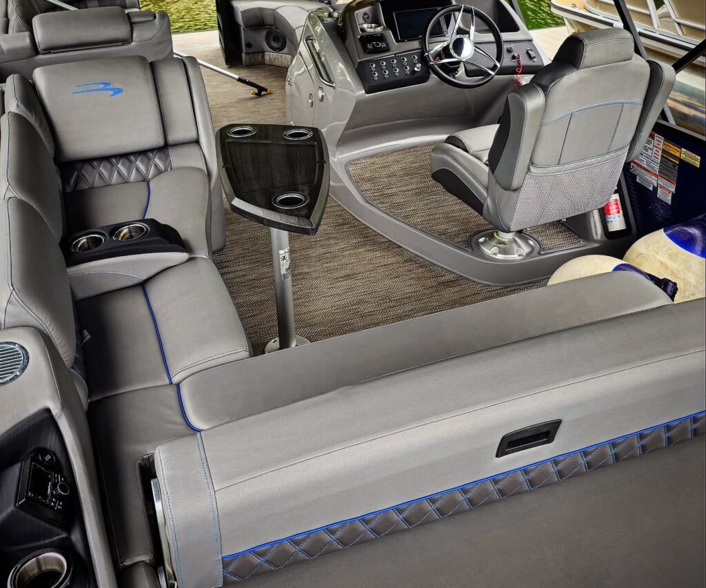Clean gray pontoon boat interior with blue-stitched upholstery, helm seat, steering console, and table at a dock