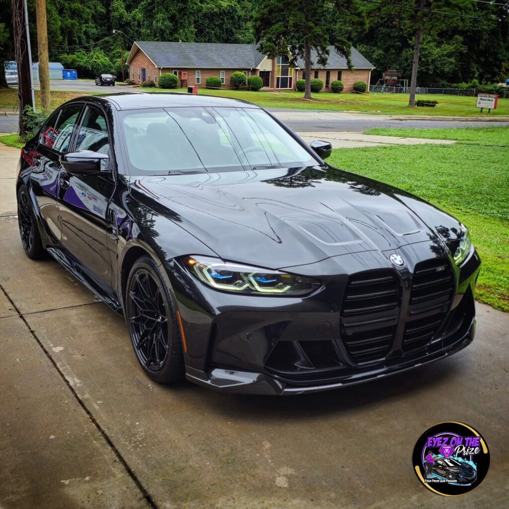 Black BMW M3 parked on a driveway with a glossy finish after exterior detailing, front three-quarter view