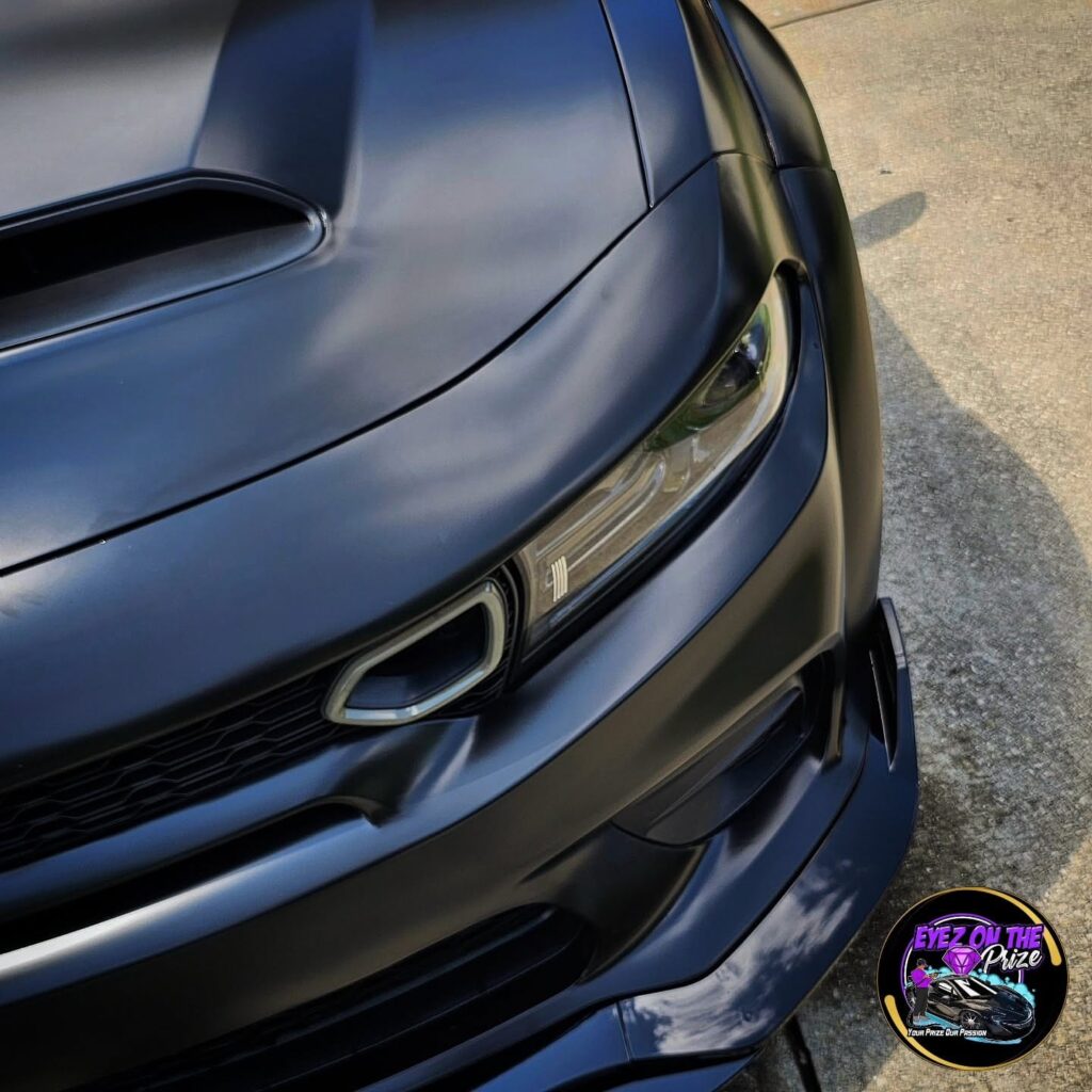Close-up of a black Dodge Charger widebody hood scoop, headlight, and front bumper after detailing.