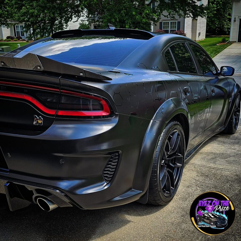 Rear quarter view of a satin black Dodge Charger Scat Pack widebody with honeycomb graphics parked in a driveway