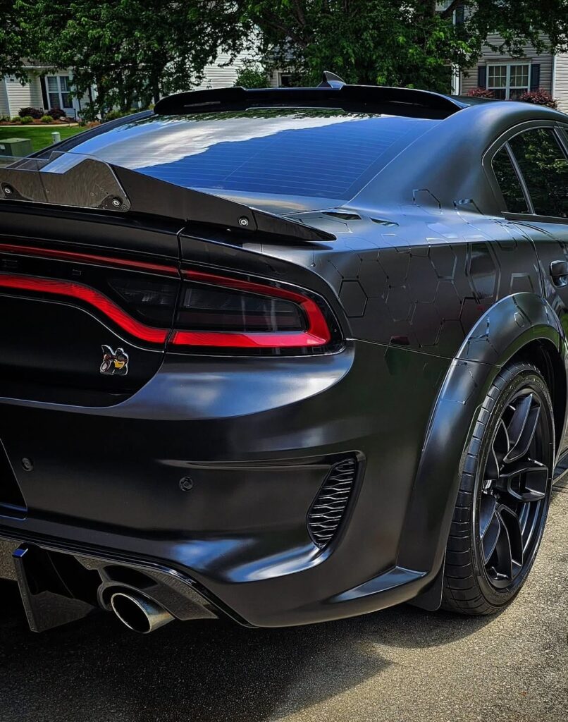 Rear quarter view of a satin black Dodge Charger Scat Pack widebody with honeycomb graphics parked in a driveway