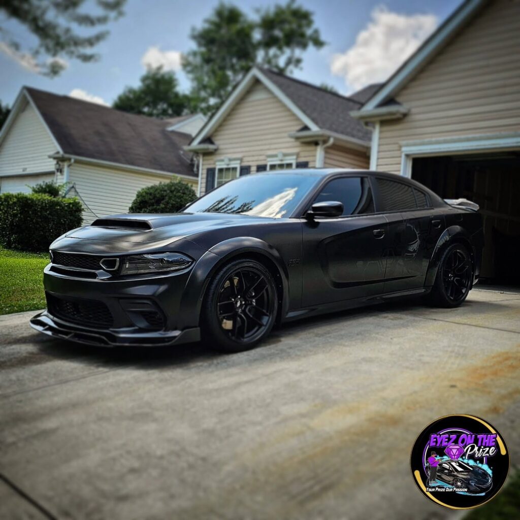 Front quarter view of a black Dodge Charger widebody with black wheels parked in a residential driveway after detailing