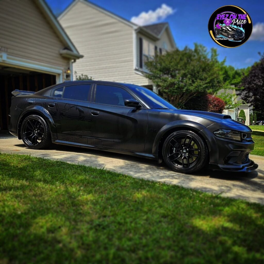 Black Dodge Charger widebody sedan with black wheels parked on a driveway after detailing, side view in sunlight.