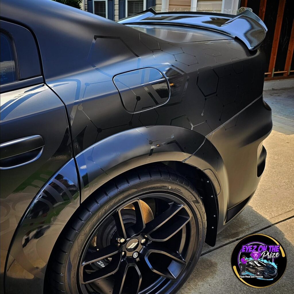 Rear quarter of a black Dodge Charger widebody with honeycomb graphics, fender flare, and black wheel after detailing