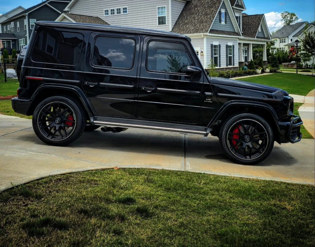 Black Mercedes-AMG G63 SUV parked in a residential driveway after detailing, side profile view with red brake calipers