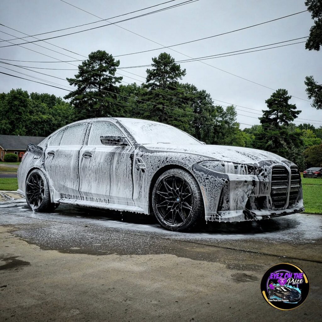 BMW M3 sedan covered in thick white foam during an exterior wash on a residential driveway in Charlotte, NC.
