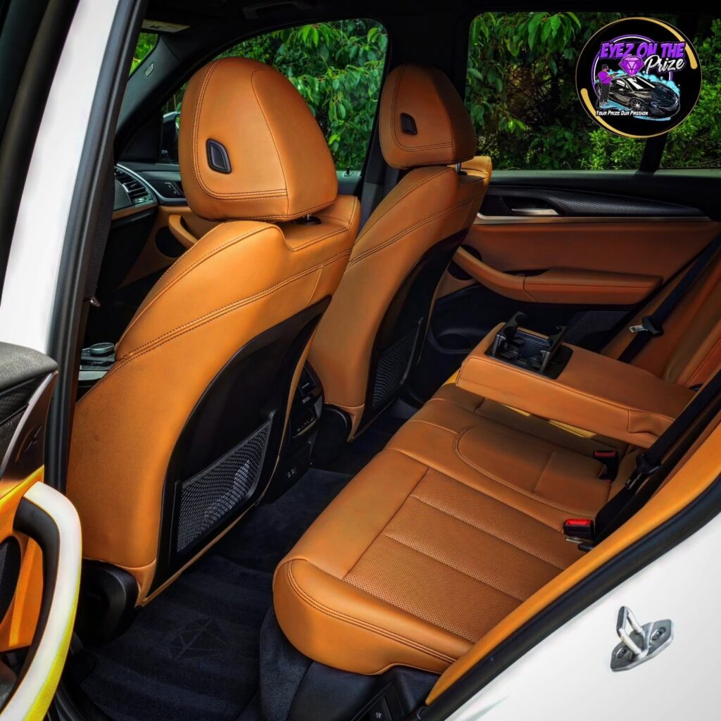 Rear seats of a white BMW X3 with cognac leather upholstery, folded center armrest, and clean black carpet.