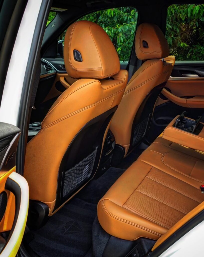 Rear seats of a white BMW X3 with cognac leather upholstery, folded center armrest, and clean black carpet.
