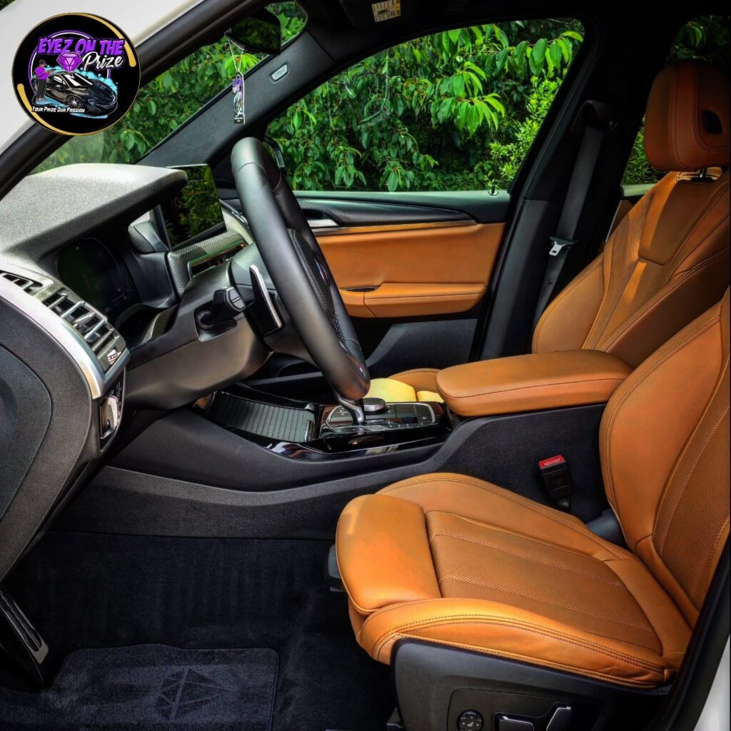 Front cabin of a white BMW X3 with cognac leather seats, black steering wheel, and clean dark carpet after detailing.