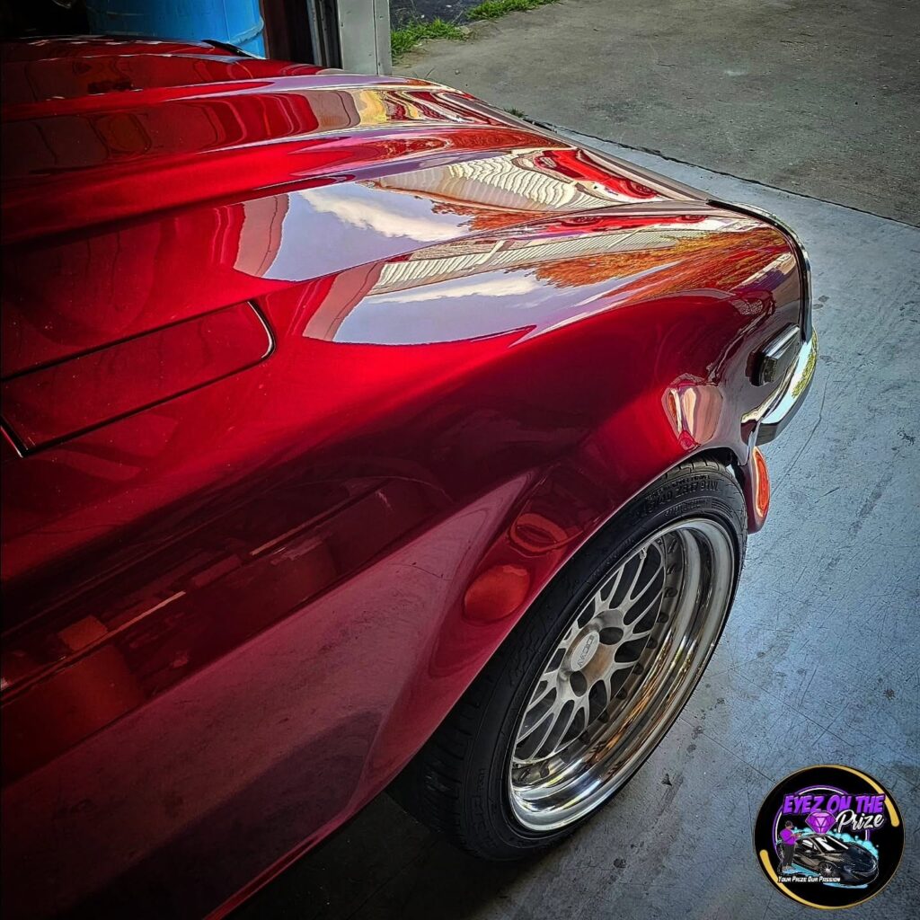 Close-up of a candy red classic car hood and front fender with a mirror-like polished finish and chrome multi-spoke wheel.
