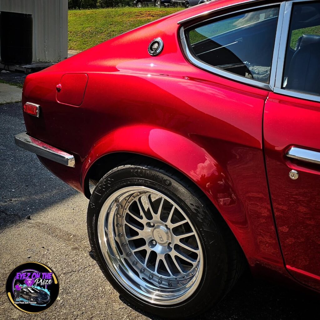 Rear quarter panel of a candy red Datsun 240Z with a polished mesh wheel and glossy paint in sunlight