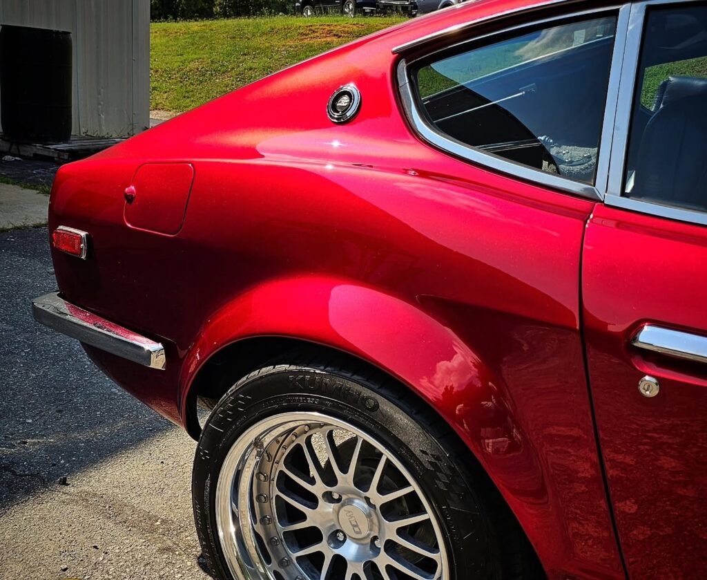 Rear quarter panel of a candy red Datsun 240Z with a polished mesh wheel and glossy paint in sunlight