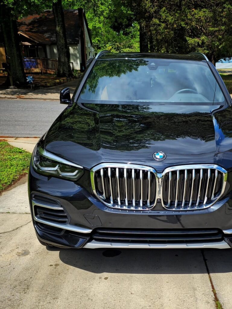 Front view of a black BMW X5 with glossy hood and chrome grille parked on a concrete driveway after detailing