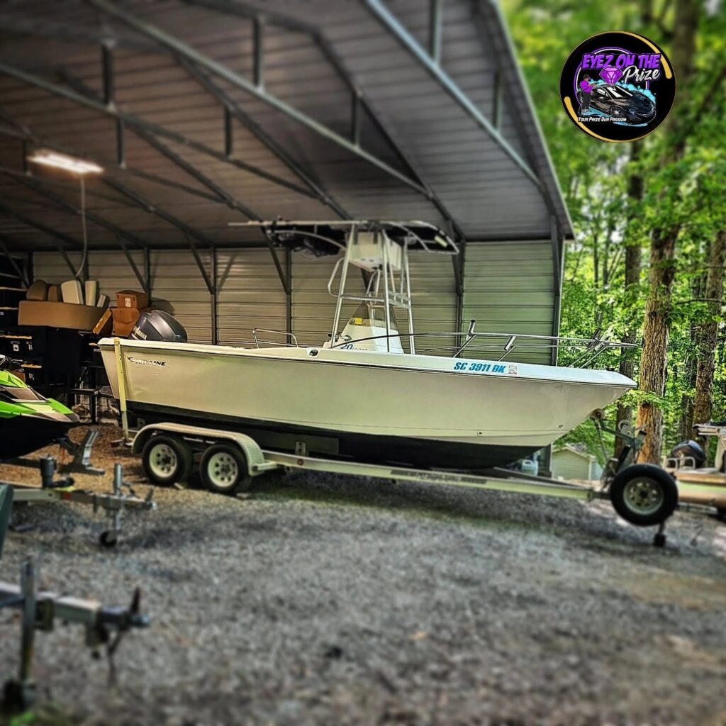 White center console fishing boat with outboard motor on a trailer under a metal carport after detailing.