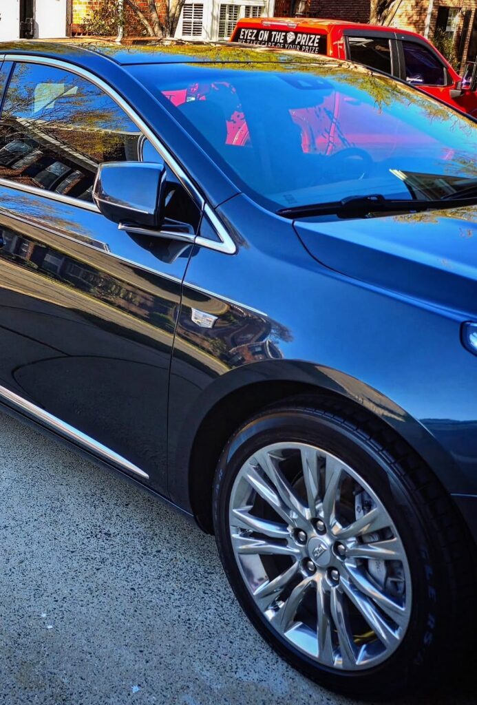 Glossy black Cadillac XTS sedan parked beside an Eyez On The Prize mobile detailing trailer in Charlotte, NC