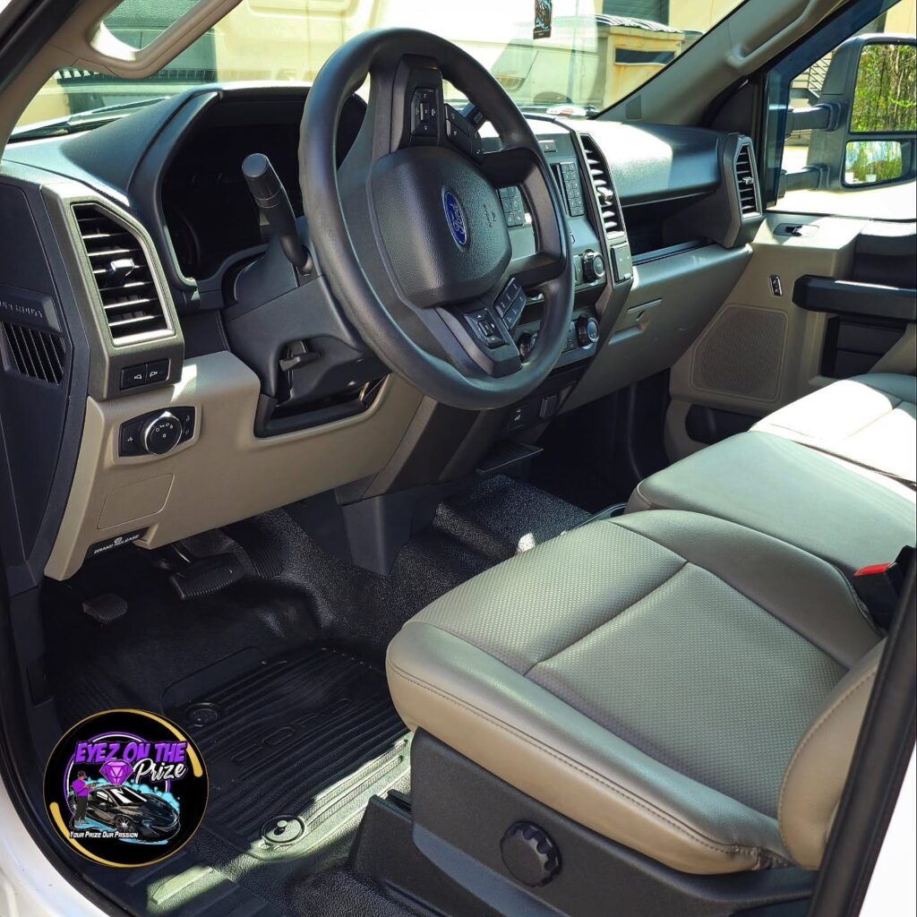 Cleaned Ford F-150 driver side interior with steering wheel, gray vinyl seats, and rubber floor mats