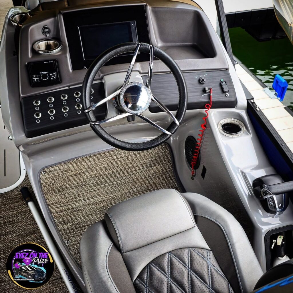 Cleaned pontoon boat helm with chrome steering wheel, gray captain's seat, and gauge console at a dock.