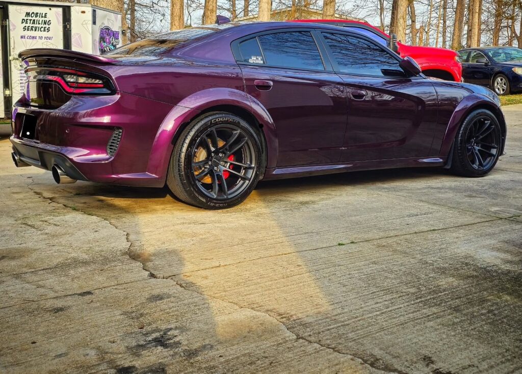 Rear quarter view of a freshly detailed purple Dodge Charger widebody parked beside a mobile detailing trailer
