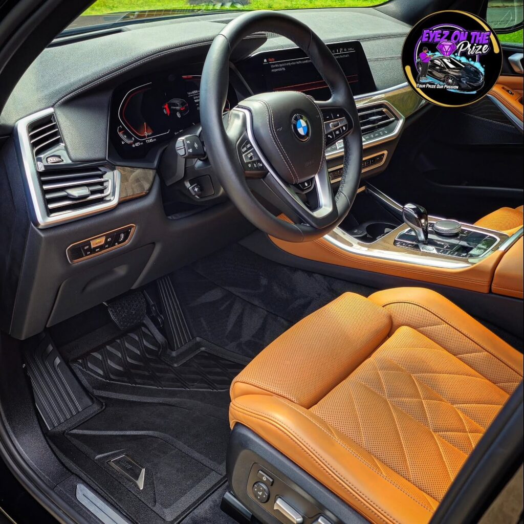 Driver cockpit of a BMW X5 with cognac leather seats, clean black floor mats, and detailed dashboard after interior