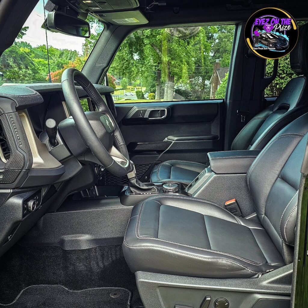 Driver side view of a Ford Bronco interior with cleaned black leather seats, steering wheel, and vacuumed carpet