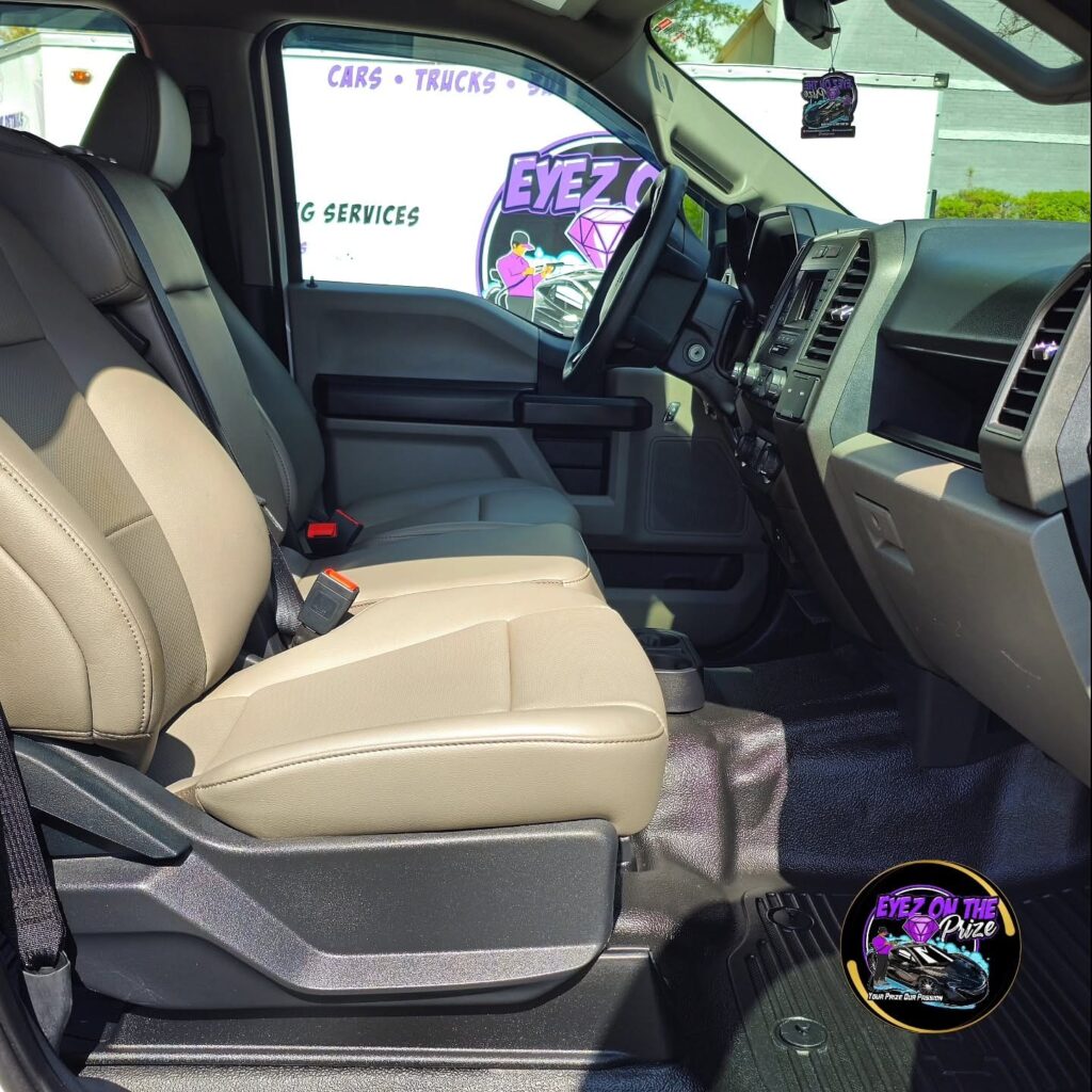 Front cabin of a Ford pickup with clean tan bench seat, black dash, and freshly detailed floor mats seen from the passenger