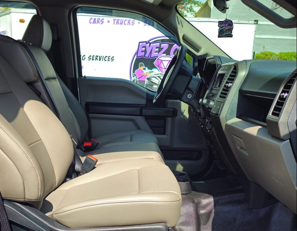 Front cabin of a Ford pickup with clean tan bench seat, black dash, and freshly detailed floor mats seen from the passenger