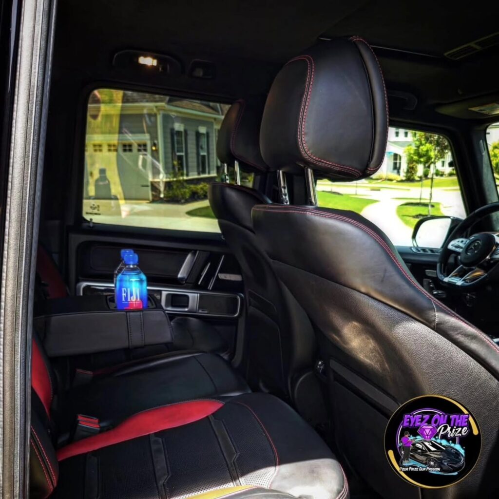 Rear seat of a Mercedes G-Wagon with black and red leather upholstery after interior detailing, viewed through the open door.