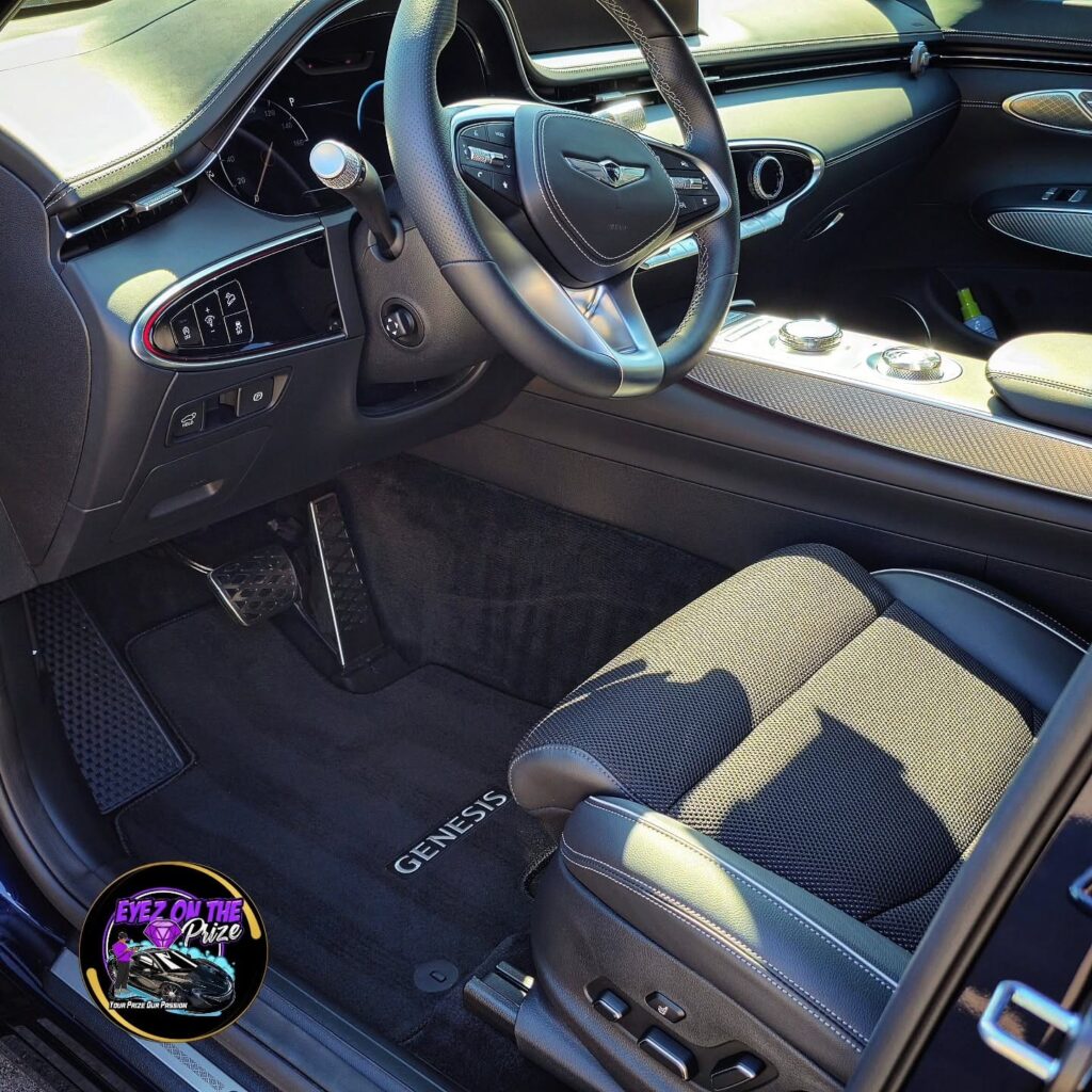 Clean driver side interior of a Genesis GV70 showing steering wheel, quilted seat, and vacuumed floor mat with Genesis