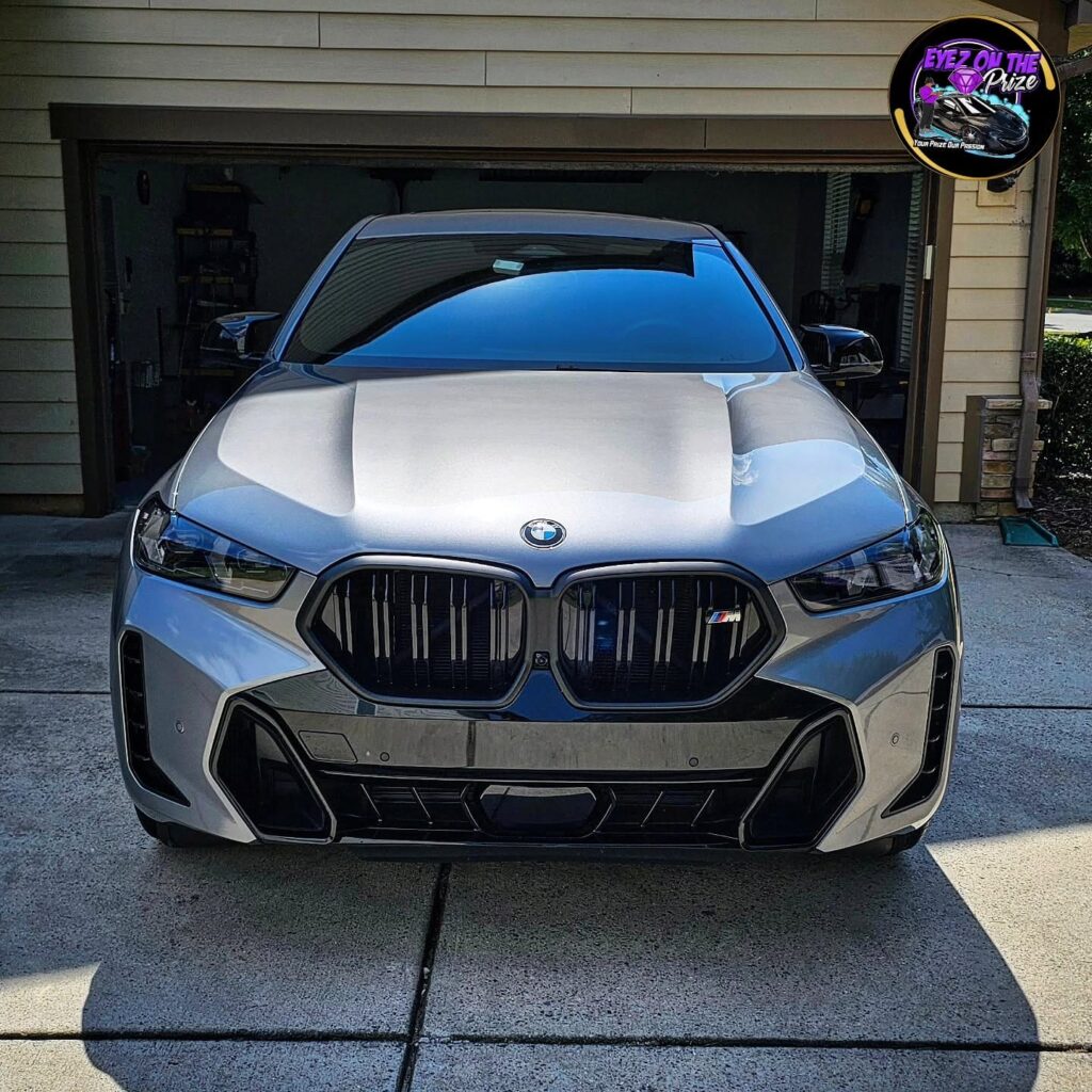 Front view of a gray BMW X6 M parked in a driveway in front of an open garage after detailing.