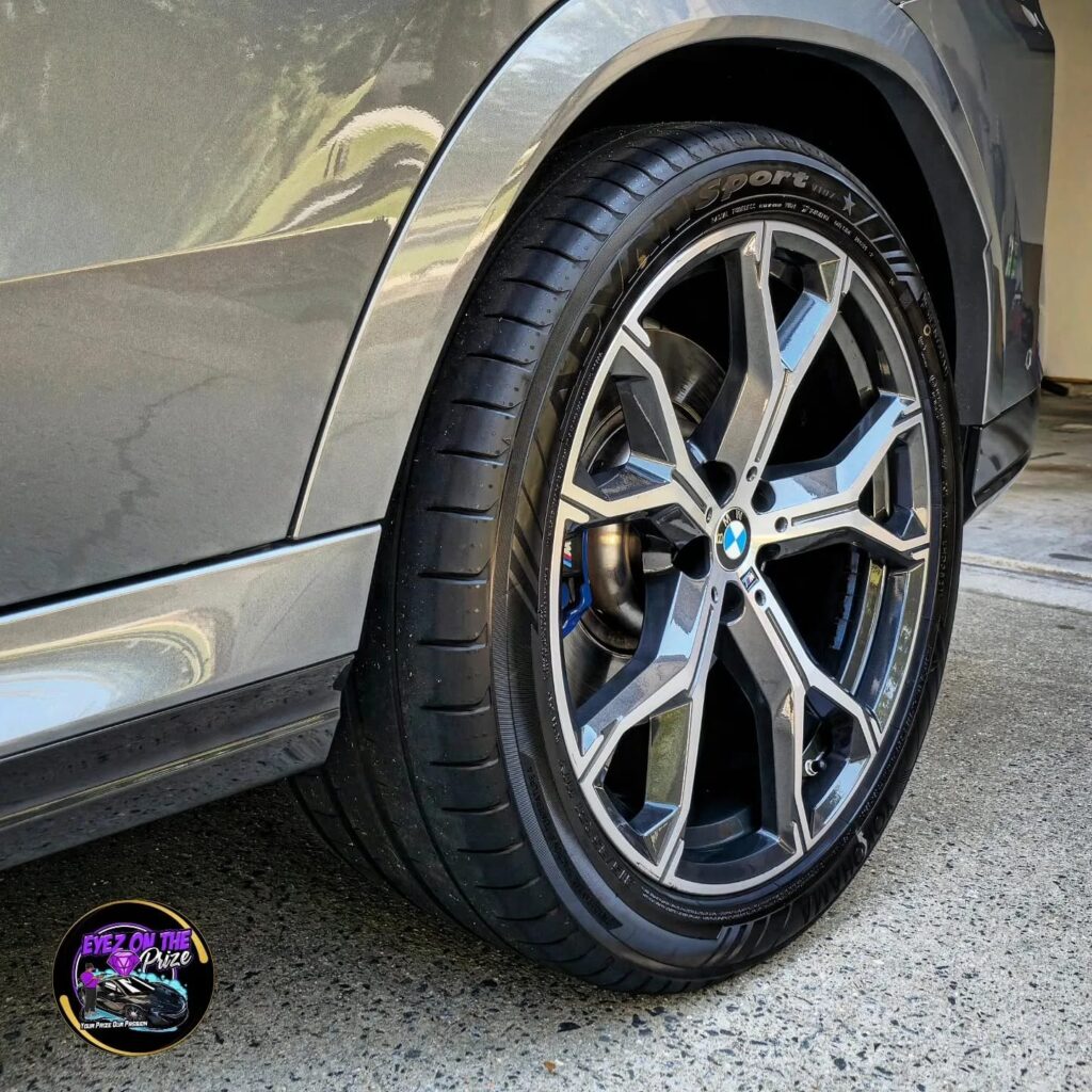 Close-up of a detailed BMW X6 M alloy wheel and glossy tire on a gray SUV in a driveway.